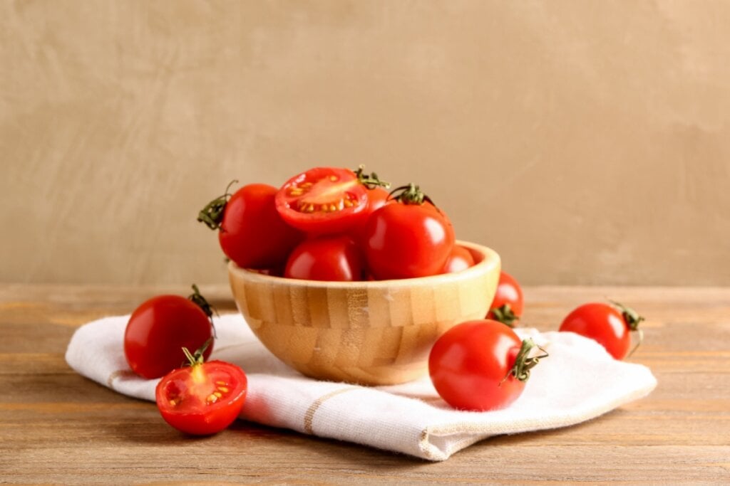 Cesto de madeira com tomates e tomates ao redor em cima de mesa de madeira