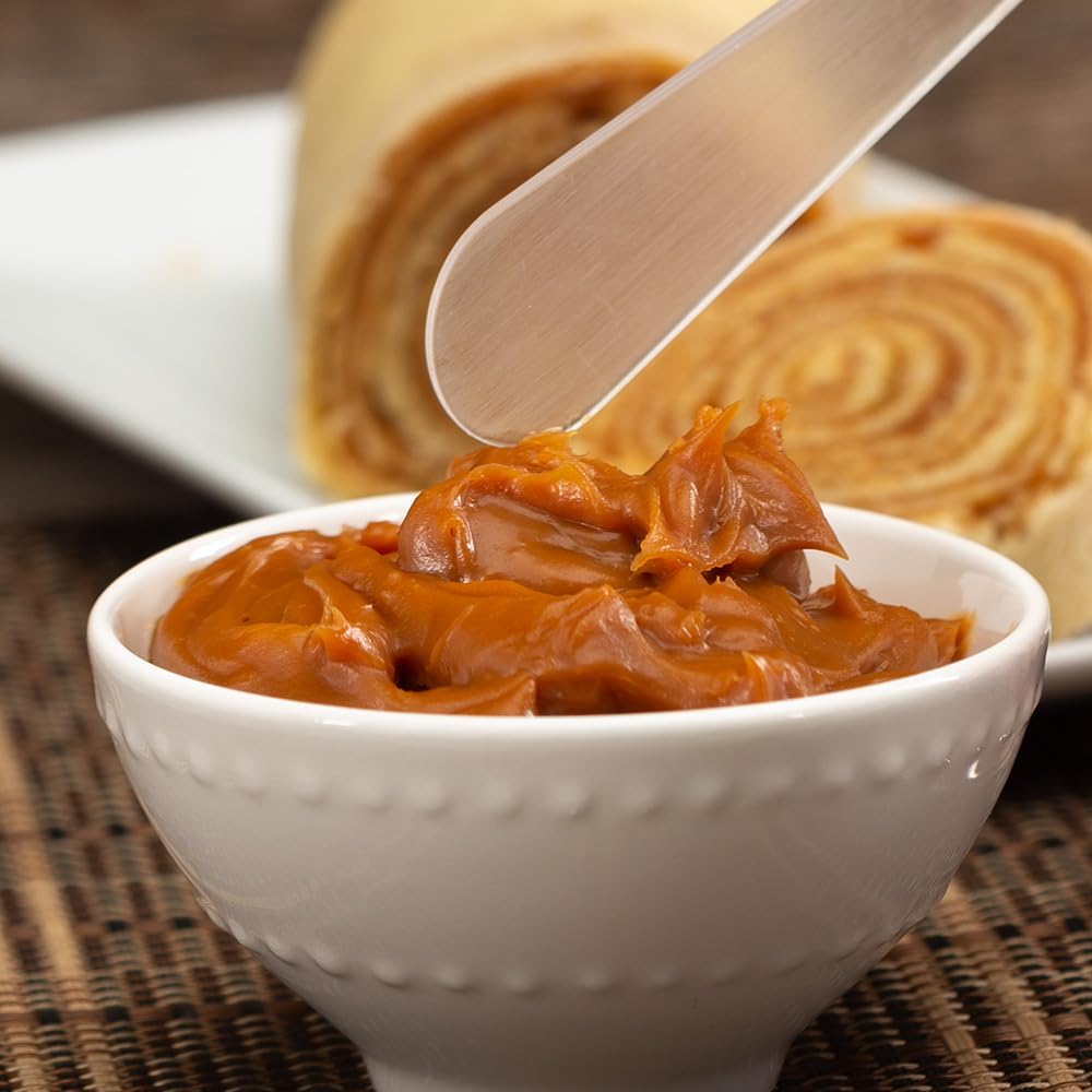 Close-up de uma colher com pasta, fundo desfocado com superfície de tecido marrom e prato branco ao fundo.